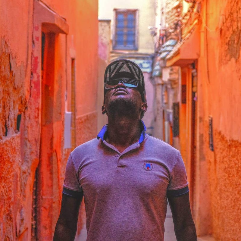 Ab Del Castro dans une ruelle colorée, casquette et lunettes de soleil